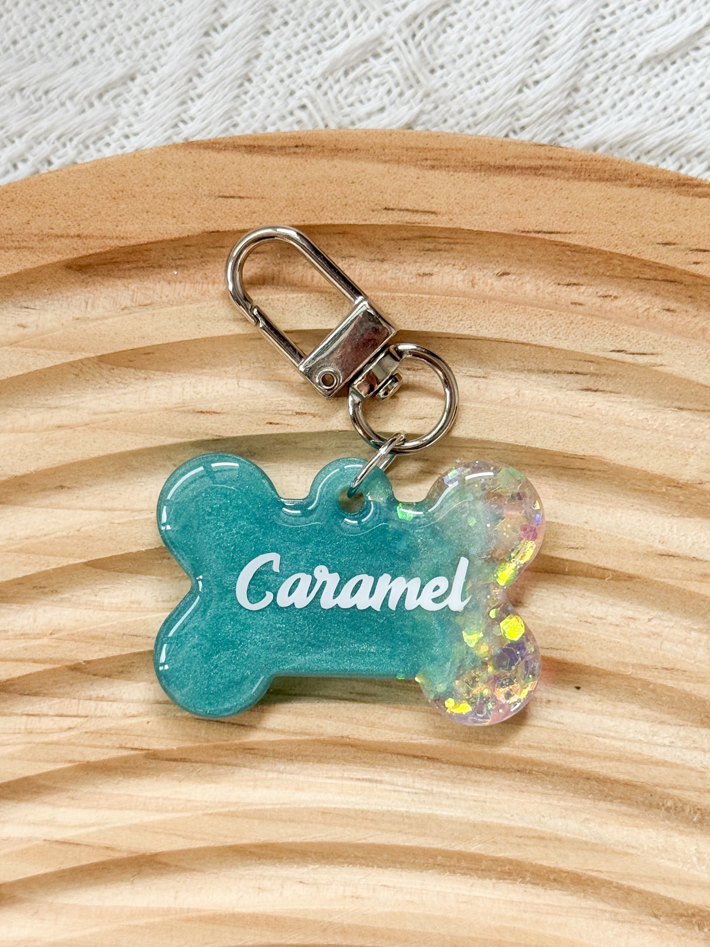 Bone-shaped teal resin pet tag with iridescent sparkle, personalized with pet's name and phone number for dogs and cats