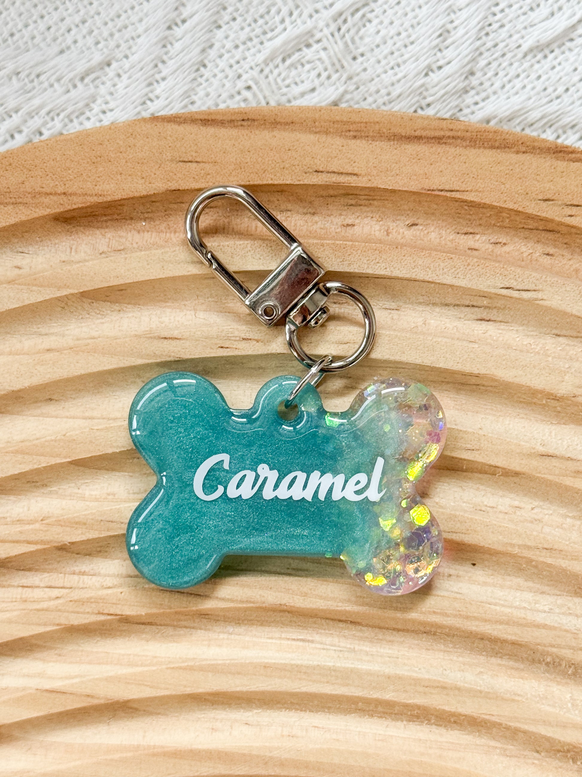 Bone-shaped teal resin pet tag with iridescent sparkle, personalized with pet's name and phone number for dogs and cats