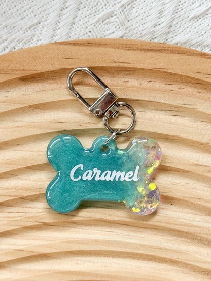 Bone-shaped teal resin pet tag with iridescent sparkle, personalized with pet's name and phone number for dogs and cats