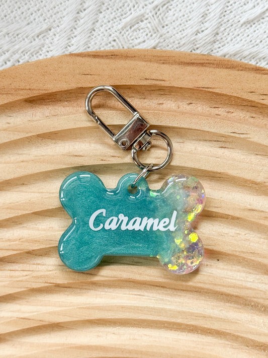 Bone-shaped teal resin pet tag with iridescent sparkle, personalized with pet's name and phone number for dogs and cats