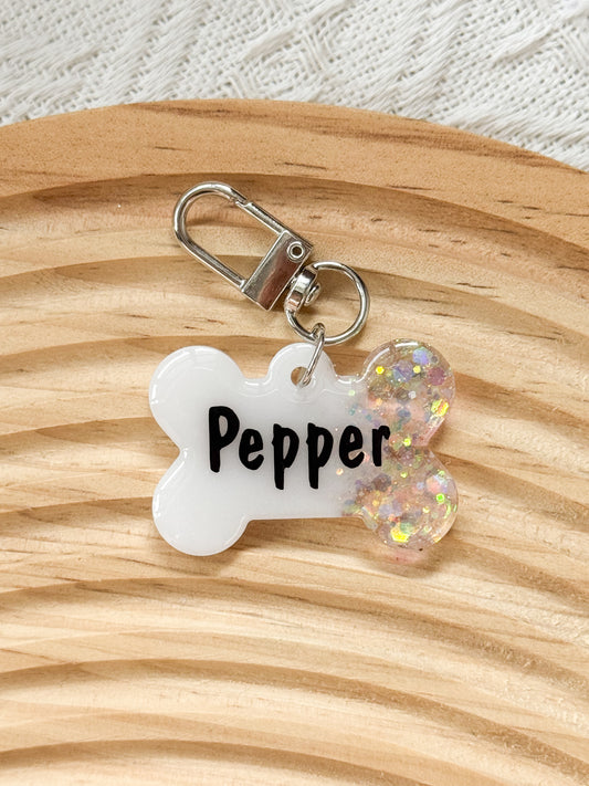 Bone-shaped white resin pet tag with iridescent sparkle, personalized with pet's name and phone number for dogs and cats