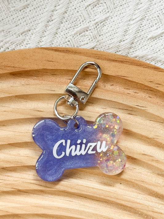 Bone-shaped violet blue resin pet tag with iridescent sparkle, personalized with pet's name and phone number for dogs and cats